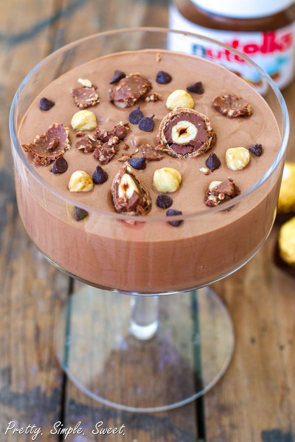 Nutella mousse in a coupe cocktail glass garnished with hazelnuts and ferrero rocher chocolates.