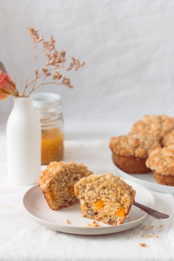 Delicious mango muffins cut in half on a white plate, exposing the bits of mango inside the muffin.