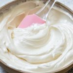 Cream Cheese Frosting swirled in a bowl with a light pink spatula stirred the mixture.