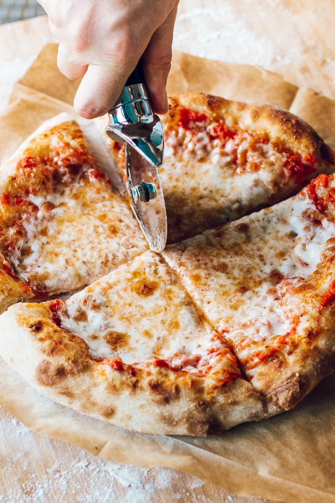 Classic Homemade Margherita Pizza with gooey, melty cheese and crushed tomato sauce being sliced with a pizza cutter.