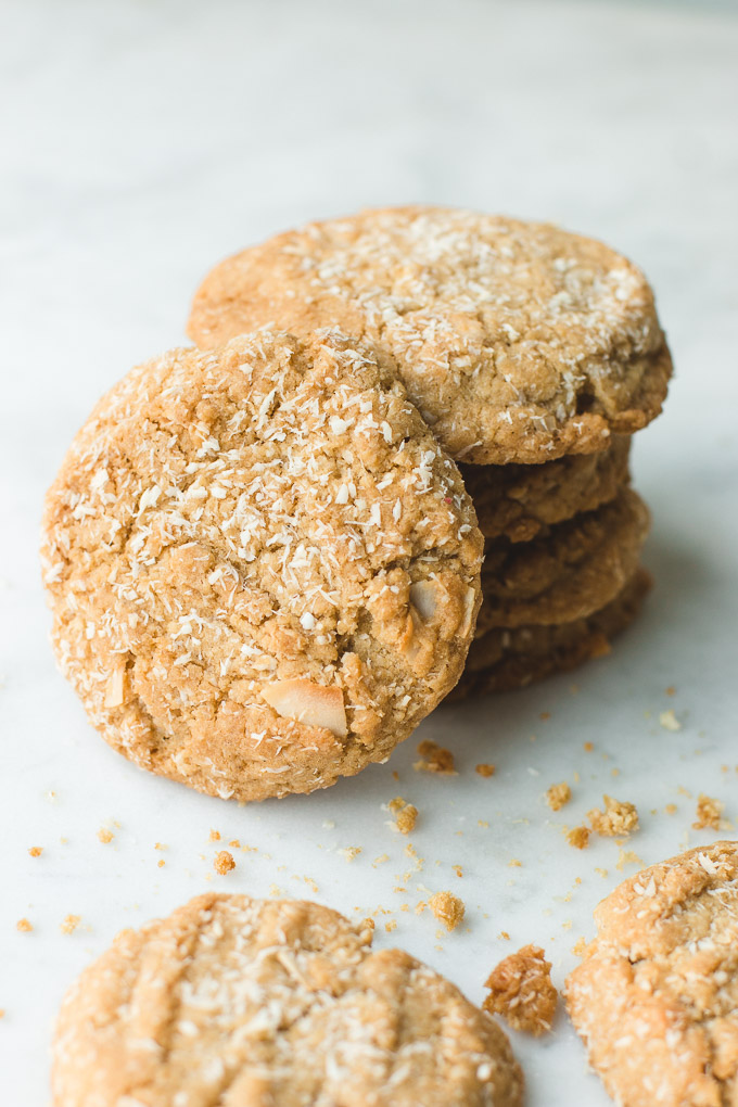 A stack of Coconut Cookies with desiccated coconut shreds adorning them and cookie crumbs scattered around.