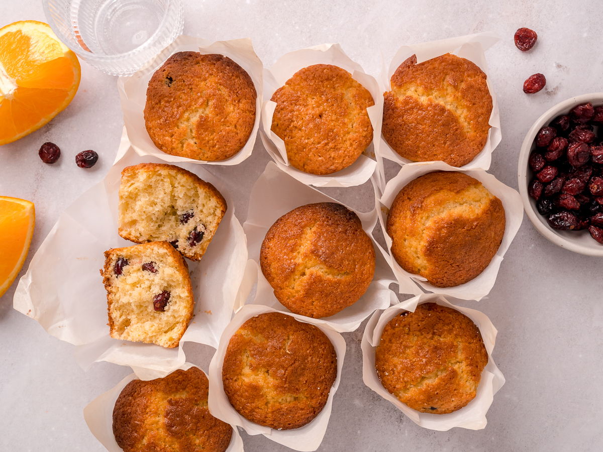 Perfectly cracked orange muffin tops with a divided muffin revealing cranberries inside.