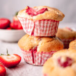 Delicious strawberry muffins stacked on top of each other with strawberries peeking out of the domed tops.