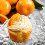 Citrusy orange cupcakes with a swirl of orange cream cheese frosting surrounded by fresh oranges.
