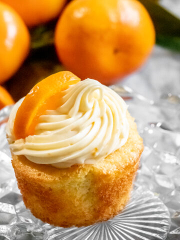 Citrusy orange cupcakes with a swirl of orange cream cheese frosting surrounded by fresh oranges.