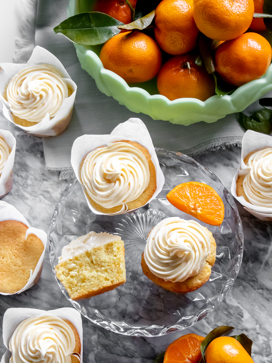 Fluffy orange cupcakes with a swirl of orange cream cheese frosting surrounded by fresh oranges.