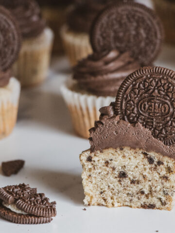 Cookies and cream cupcake split in half, topped with black cocoa cream cheese frosting and an oreo garnish.