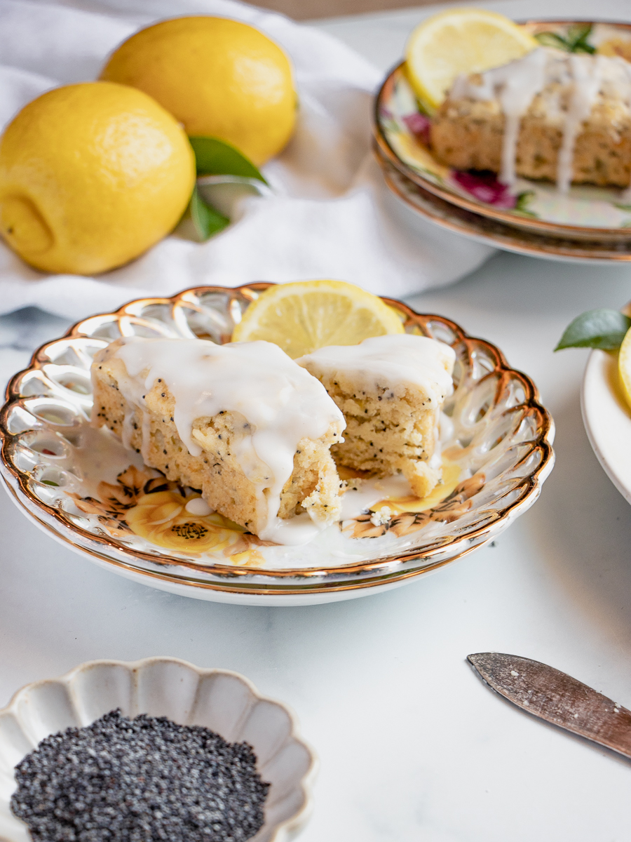 Moist lemon poppy seed scone broken in half to show its texture, topped with icing and styled with fresh citrus.