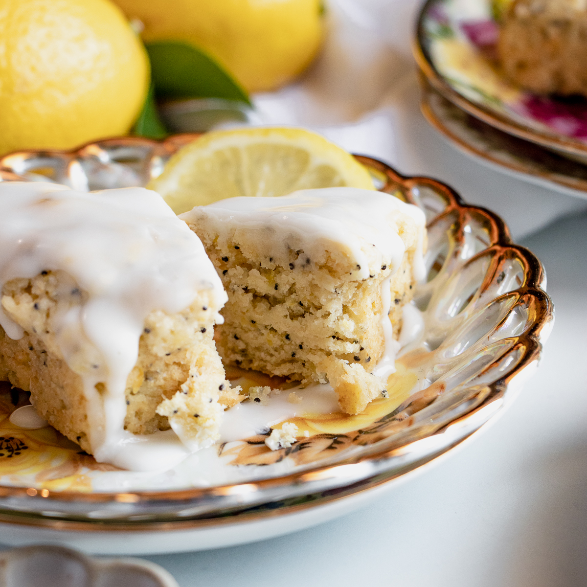 Moist lemon poppy seed scone broken in half to show its texture, topped with icing and styled with fresh citrus.