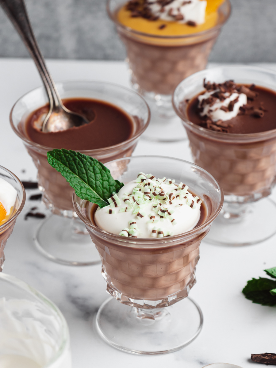 Chocolate panna cotta served in individual dessert dishes with various toppings like whipped cream and fruit curd.