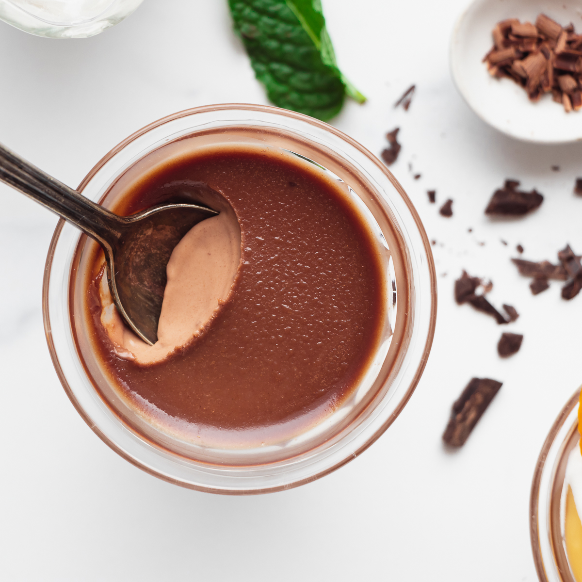 A spoon digging into a glass dish of chocolate panna cotta.