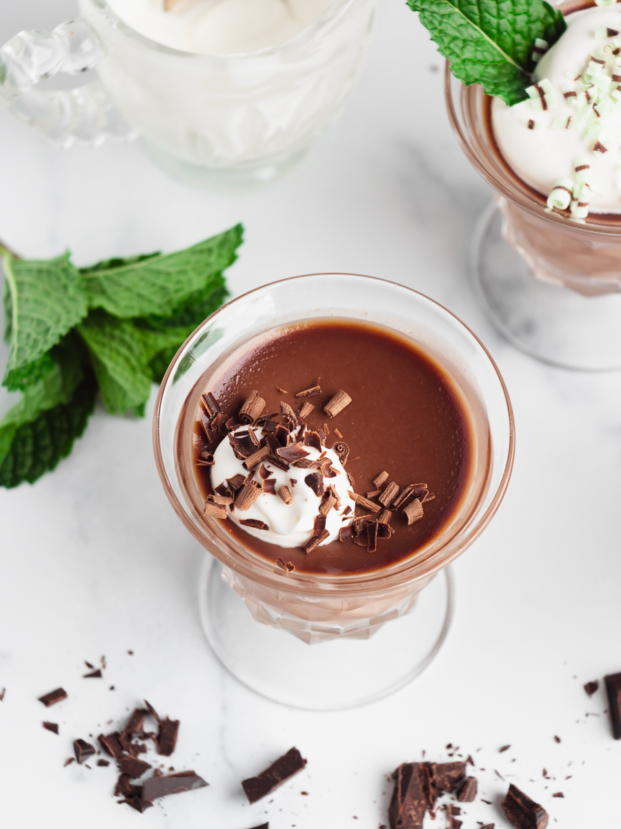 Dish of chocolate panna cotta with a dollop of whipped cream, chocolate shavings, and a spring of mint.