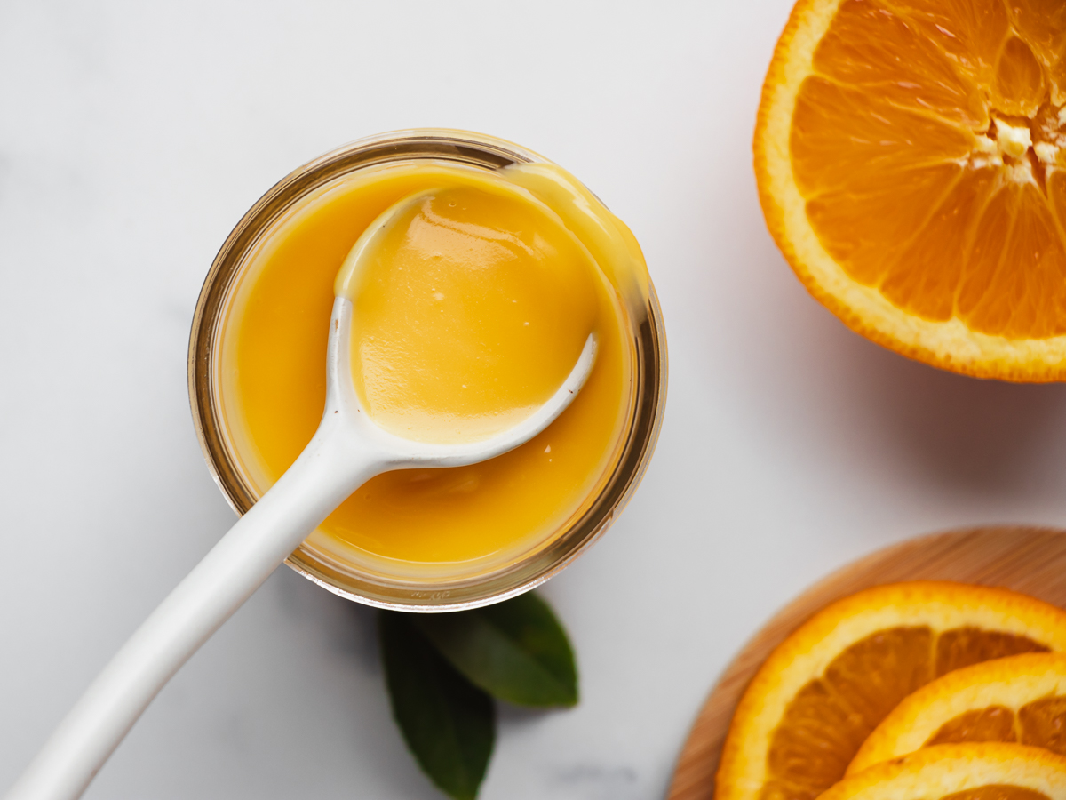 Jar of orange curd with a spoonful of curd, garnished with oranges.