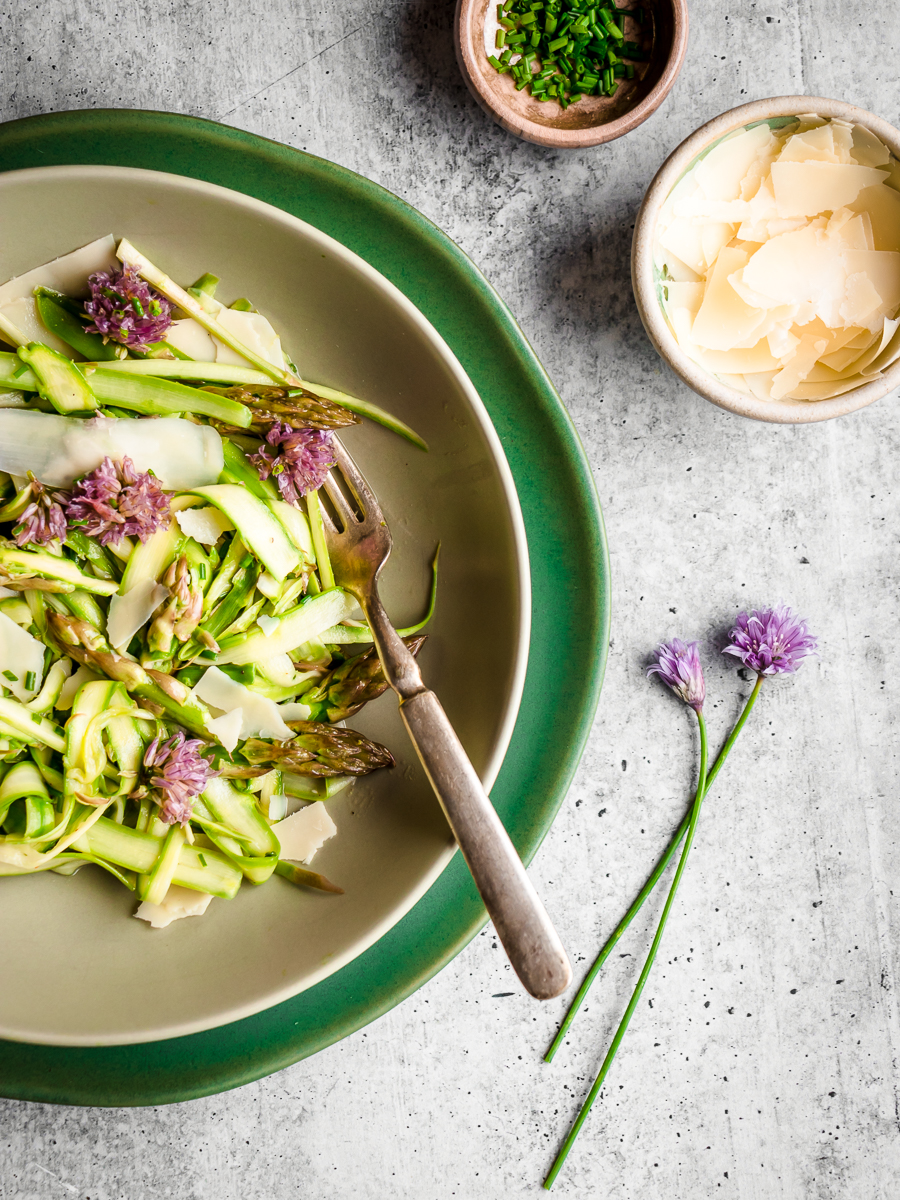 Plated asparagus salad made with parmesan cheese and chives, with fork and chive blossoms on the side.