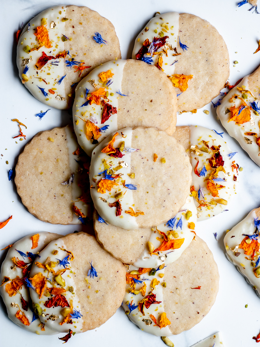 Shortbread cookies decorated with white chocolate, pistachio, and dried orange and blue flower petals.